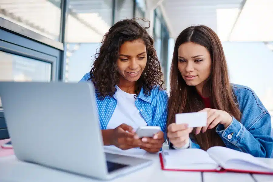 Two young women looking at a phone and laptop wondering, “Can two people have the same phone number?